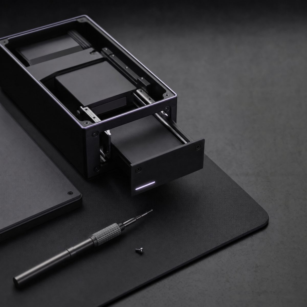 Black anodized enclosure with an open drawer, purple accent light, and a precision screwdriver